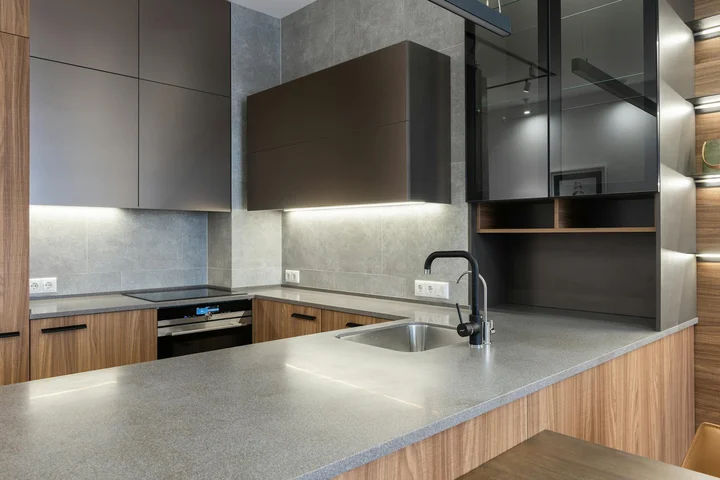 Contemporary kitchen with gray quartz countertops, wooden lower cabinets, and a stainless steel sink on an island.