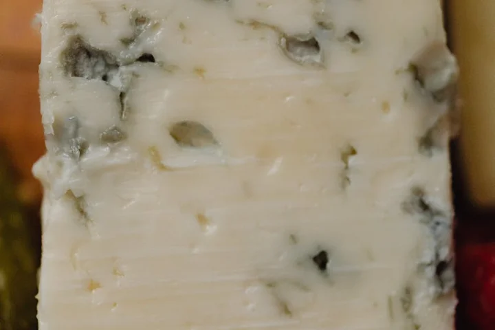 Close-up of mold growth on a cheese surface with white and blue-green mold patches.