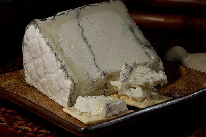 Block of white cheese with mold streaks on a wooden tray.