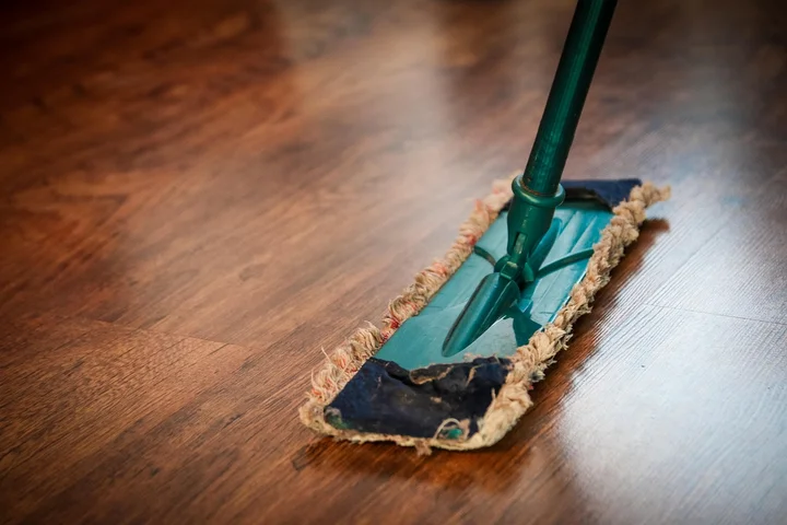 Green flat mop on a wooden floor with a frayed cleaning pad