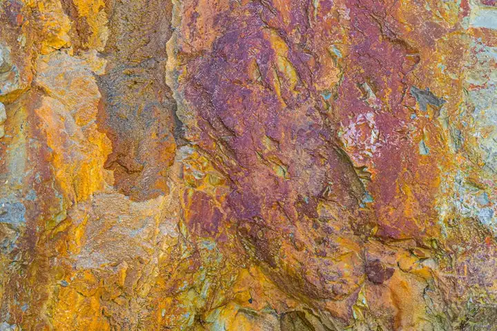 Close-up of a rugged rock surface with orange, yellow, and purple hues.