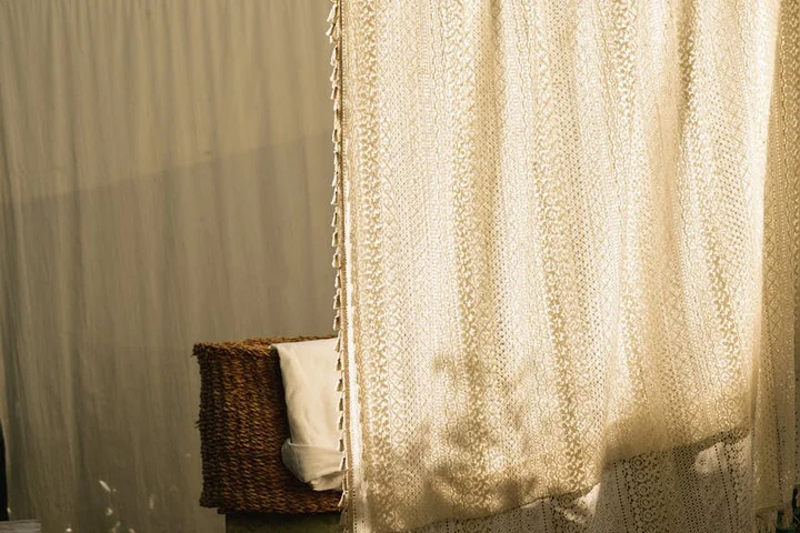 A cozy interior with a wicker chair and patterned cream-colored curtains bathed in warm light.