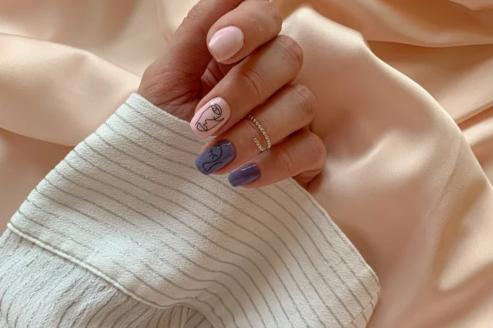 Close-up of a hand with pastel pink and lavender manicure resting on light, striped fabric.