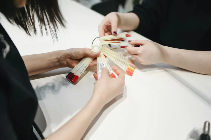Close-up of hands holding multiple nail polish color swatches over a white table.