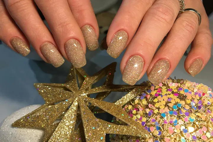 Close-up of glittery gold nail polish on manicured nails beside a glittery star ornament.