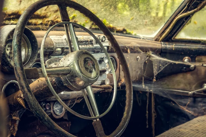 Interior of an old, dusty car with a cracked steering wheel and grimy dashboard, illustrating automotive grime and surface stains.