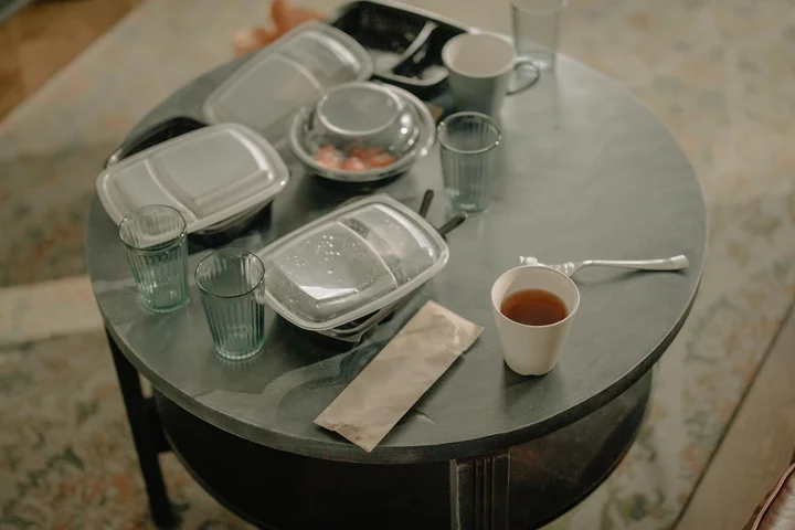 Round coffee table with several plastic storage containers and lids, some with dried orange stains, a few drinking glasses, and a cup on the table.