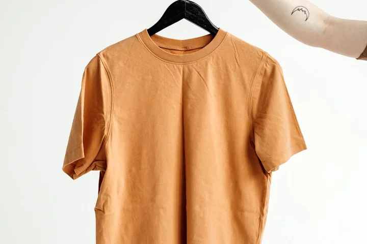 Orange-brown T-shirt on a black hanger against a light background.