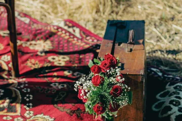 Red rose bouquet on a wooden bench beside a patterned outdoor rug outdoors