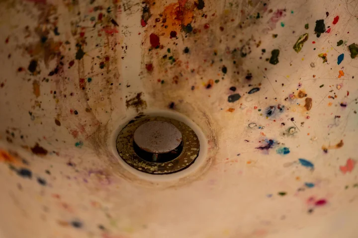 Sink basin covered in multicolored paint splatters around a central drain.