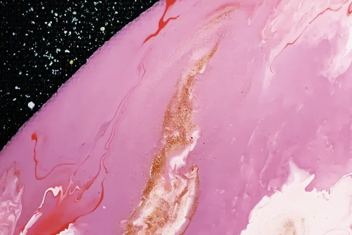 Close-up of a pink paintball stain with red and gold streaks on a dark surface, illustrating a stubborn stain.