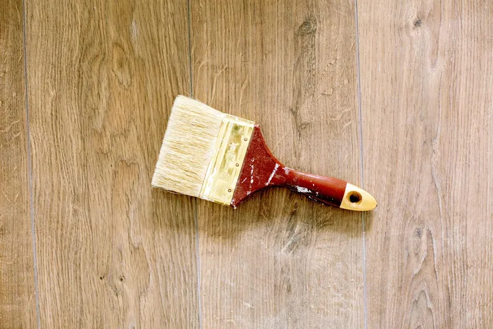 Paintbrush on a wooden floor, representing the final wash stage in paint stain removal.