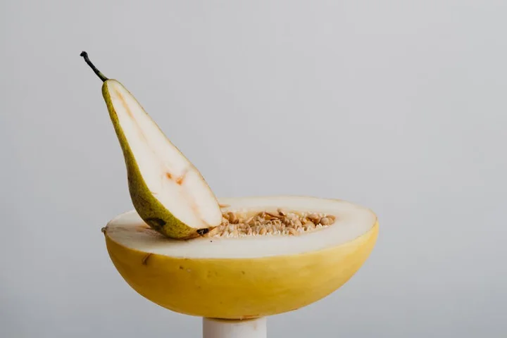 A halved yellow pear resting on a white pedestal against a pale gray background.