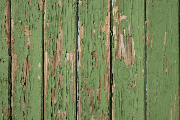 Close-up of weathered wooden boards with green peeling paint and exposed wood grain