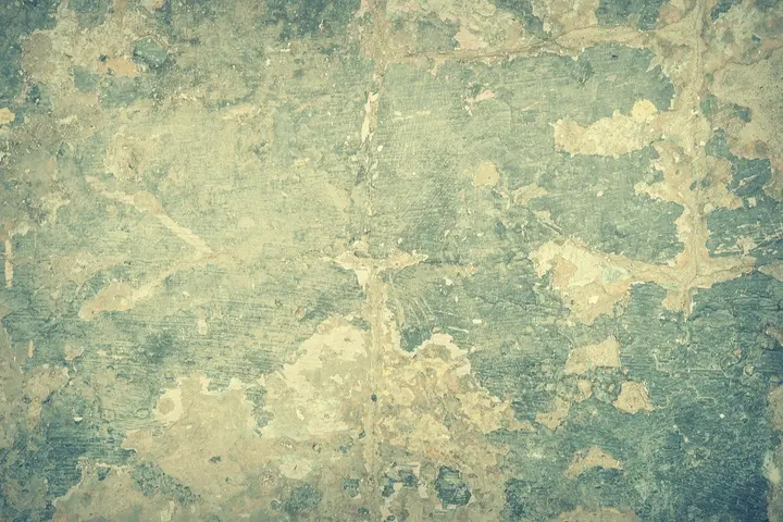 Close-up of a textured wall with blue-green peeling paint and exposed layers.