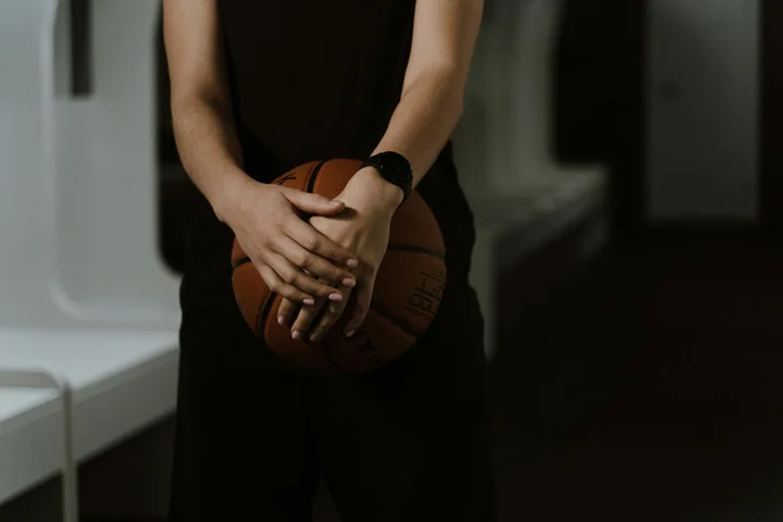 Person in dark athletic clothing holding a basketball in an indoor setting.