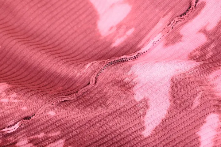 Close-up of pink tie-dye fabric with white patches and visible ribbed texture