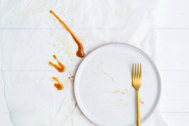 White plate with orange sauce stains and a gold fork on a white table.