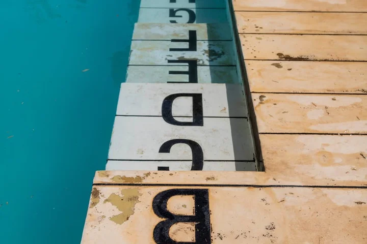 Close-up of beige pool deck tiles along the waterline with brown rust stains and blue pool water visible to the left.
