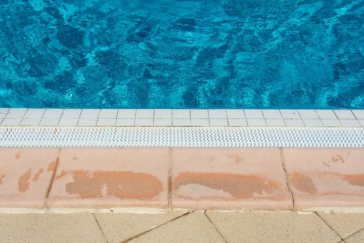 Close-up of stained pool coping tiles along the edge of a blue swimming pool