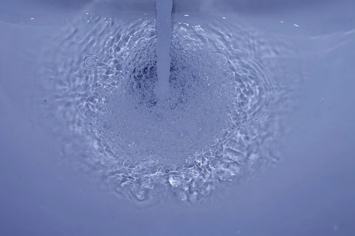 Blue porcelain sink drain with swirling water and bubbles