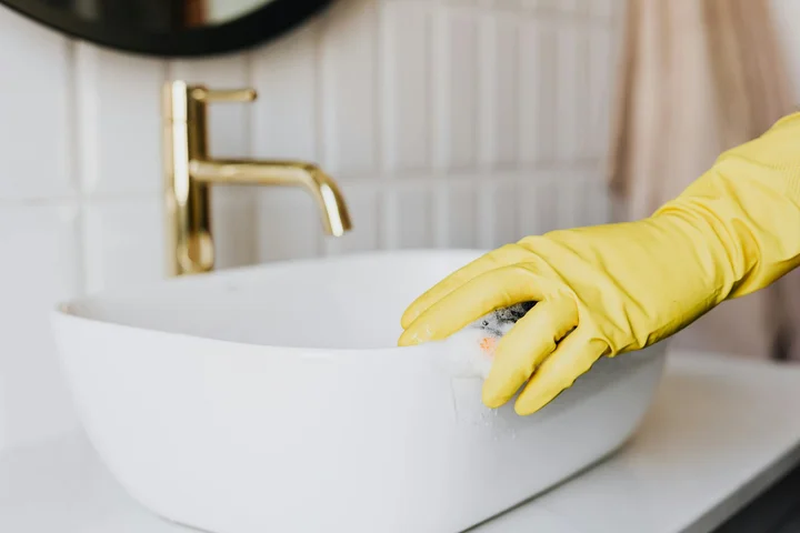 Person wearing yellow rubber gloves scrubbing a white porcelain sink