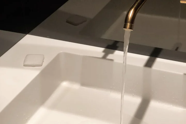 Close-up of a white porcelain sink with a brass faucet, water running into the basin.
