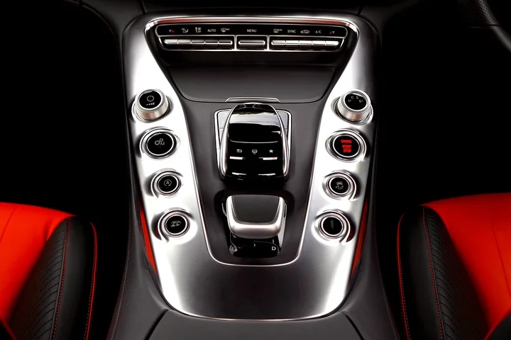 Close-up of a luxury car center console with metallic trim and red leather seats, highlighting premium interior materials.