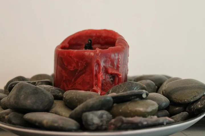 Red candle with melted wax resting in a holder on a plate surrounded by smooth stones.