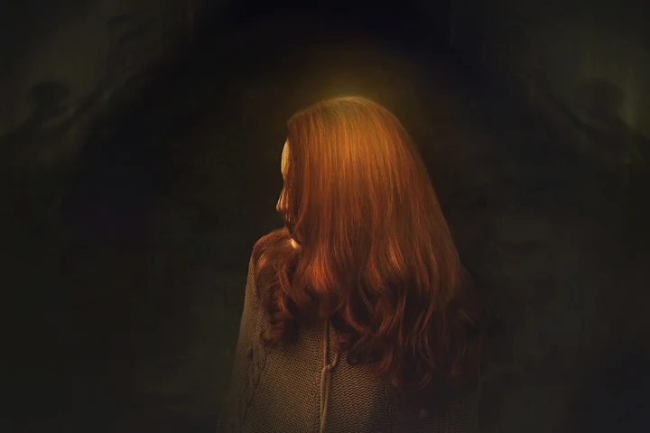 Back view of a person with long red hair in a dim, warm-lit setting