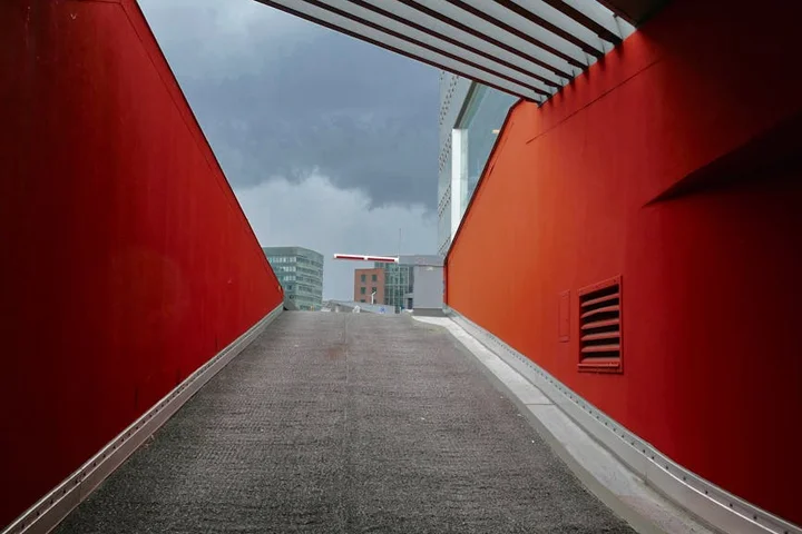 Red-walled concrete ramp leading to an outdoor street under an overcast sky