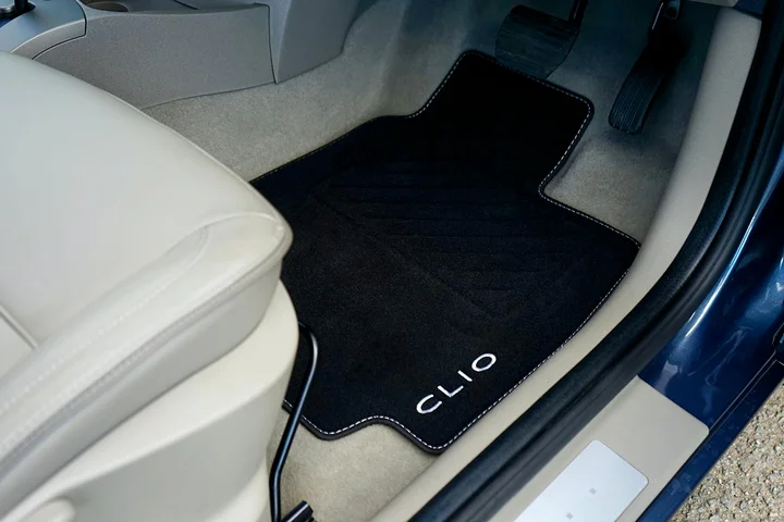 A Renault Clio's interior showing a black floor mat labeled CLIO on the driver's side with the surrounding light-gray carpet.