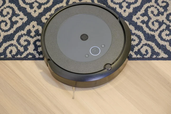 Robotic vacuum cleaner on a wooden floor near a patterned rug