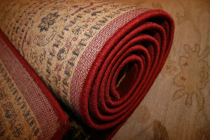 Rolled decorative carpet with a red edge on a beige patterned floor