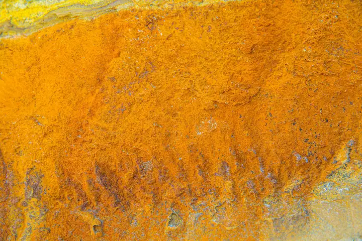 Close-up of an orange rust stain on a tile surface, showing rust spreading across the tile and grout.