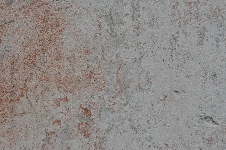 Close-up of reddish-brown rust stains on a gray, concrete-like surface, illustrating iron oxidation.