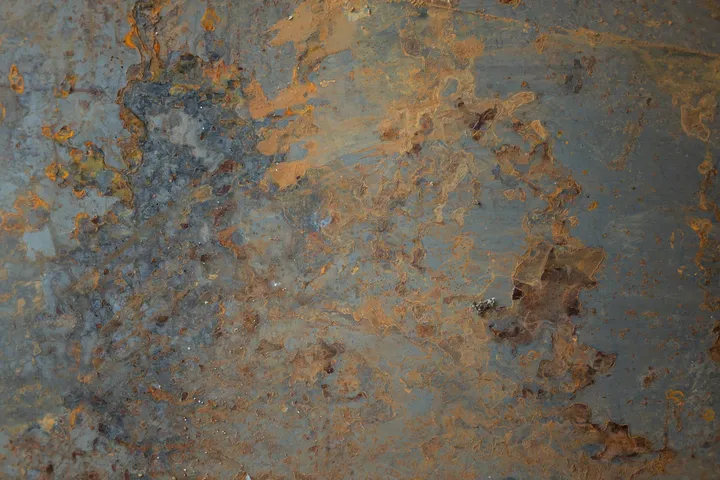 Close-up of a rusted metal surface with blue-gray background and orange-brown rust patches.