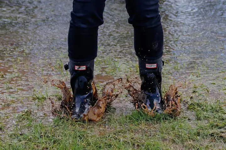Two black UGG-style boots standing in a muddy puddle with water splashing around.