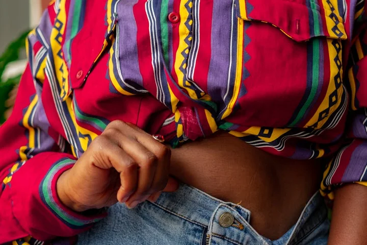 Close-up of a person wearing a colorful striped shirt and blue jeans, lifting the shirt at the waist.