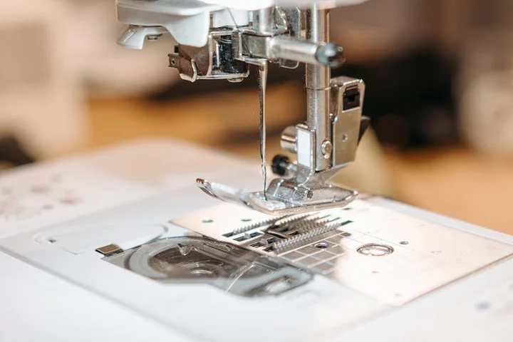 Close-up of a sewing machine needle and presser foot over fabric, showing stitching and fabric texture.