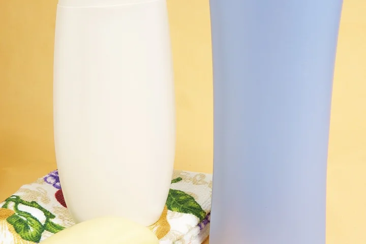 Two haircare bottles (one white, one blue) sit on a towel with a yellow background, illustrating post-workout hair care.