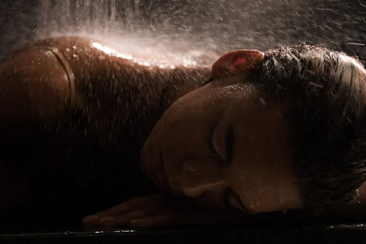 Person lying on their side under a shower spray with water droplets cascading around
