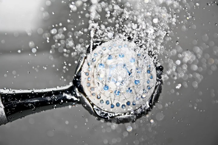 Handheld showerhead spraying water with numerous droplets to illustrate hard water on glass surfaces.