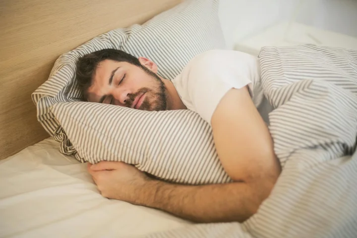 Person sleeping on a bed with striped pillows and white sheets