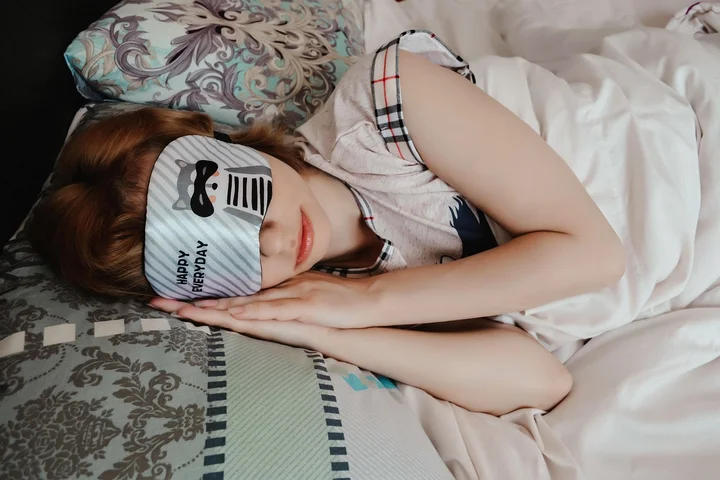 Woman sleeping in bed with a striped sleep mask covering her eyes.