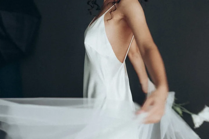 Side view of a person in a white sleeveless dress twirling a sheer veil.