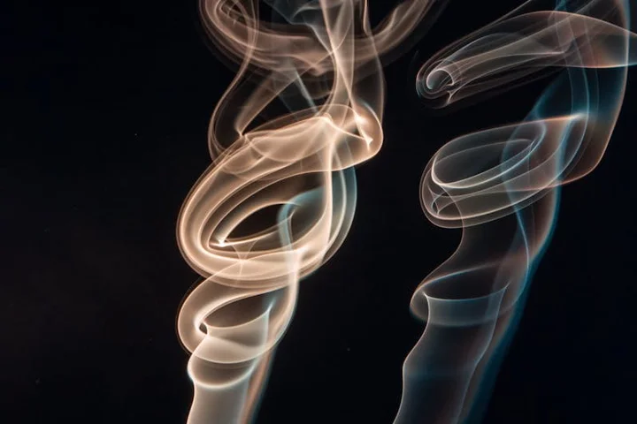 Abstract wisps of smoke curling in a dark background, representing the hidden costs of odor-removal methods.