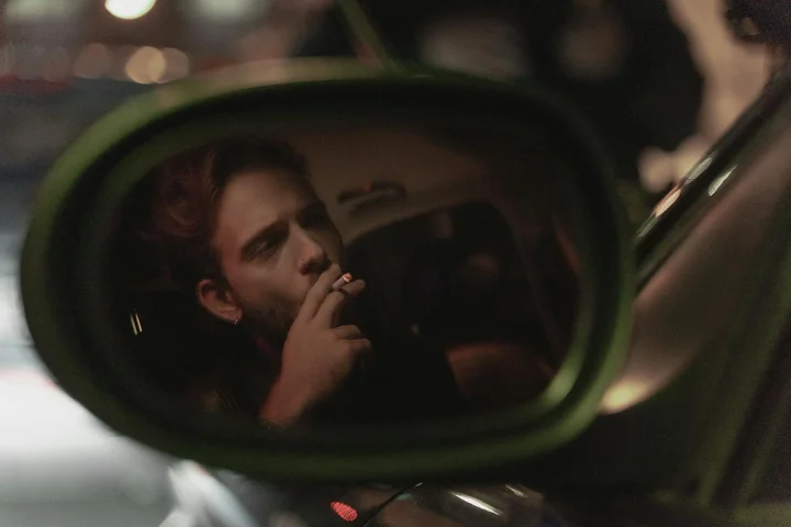 Person smoking inside a car, visible in the side-view mirror, highlighting lingering odors.