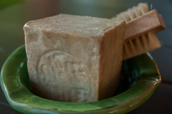 Bar of soap on a green dish with a small scrub brush beside it.