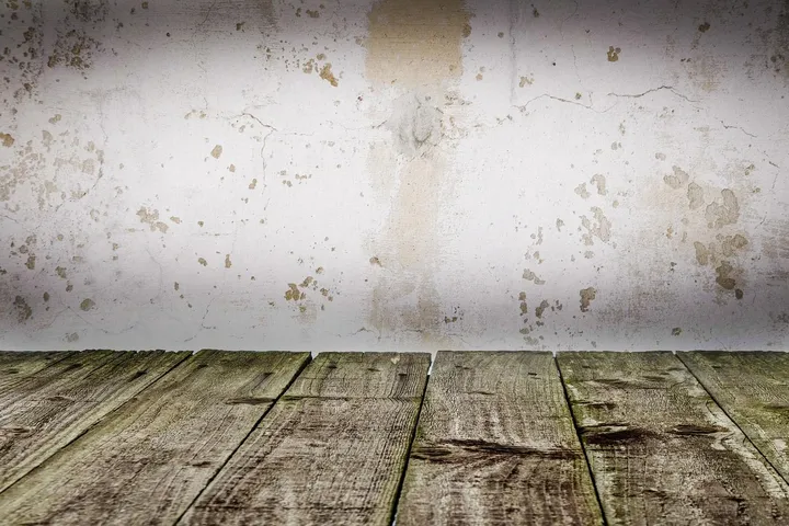 Interior scene showing a white wall with soot stains and a weathered wooden floor